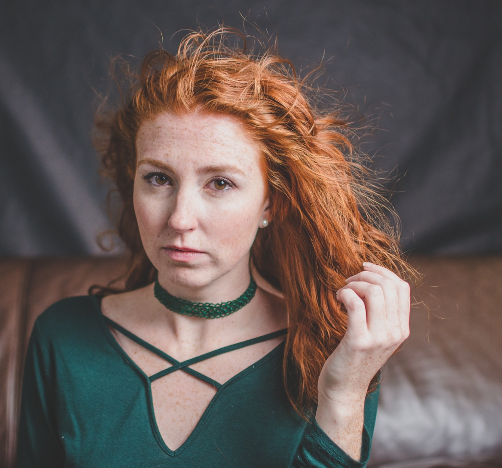 Moira from Meadowsweet. Woman with pale skin and freckles, wavey red hair, and brown eyes, wearing a green laced top and matching choker.